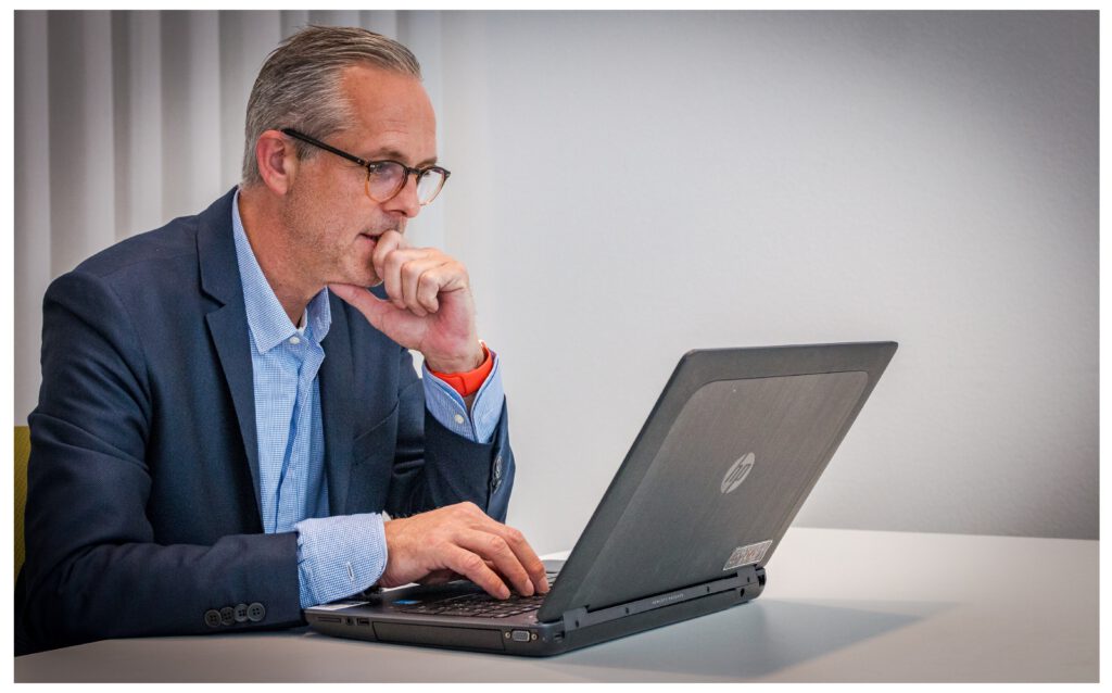 Mann im besten Alter sitzt am Laptop und spricht im Online Meeting mit Kollegen