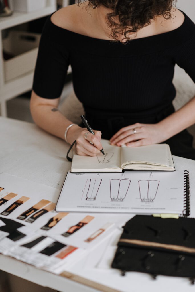 Frau sitzt am Notizblock und zeichnet Modellzeichnung von Sommerkleidern am Schreibtisch